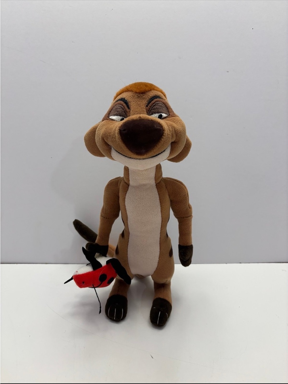 Disney The Lion King Timon plush toy holding a small red ladybug